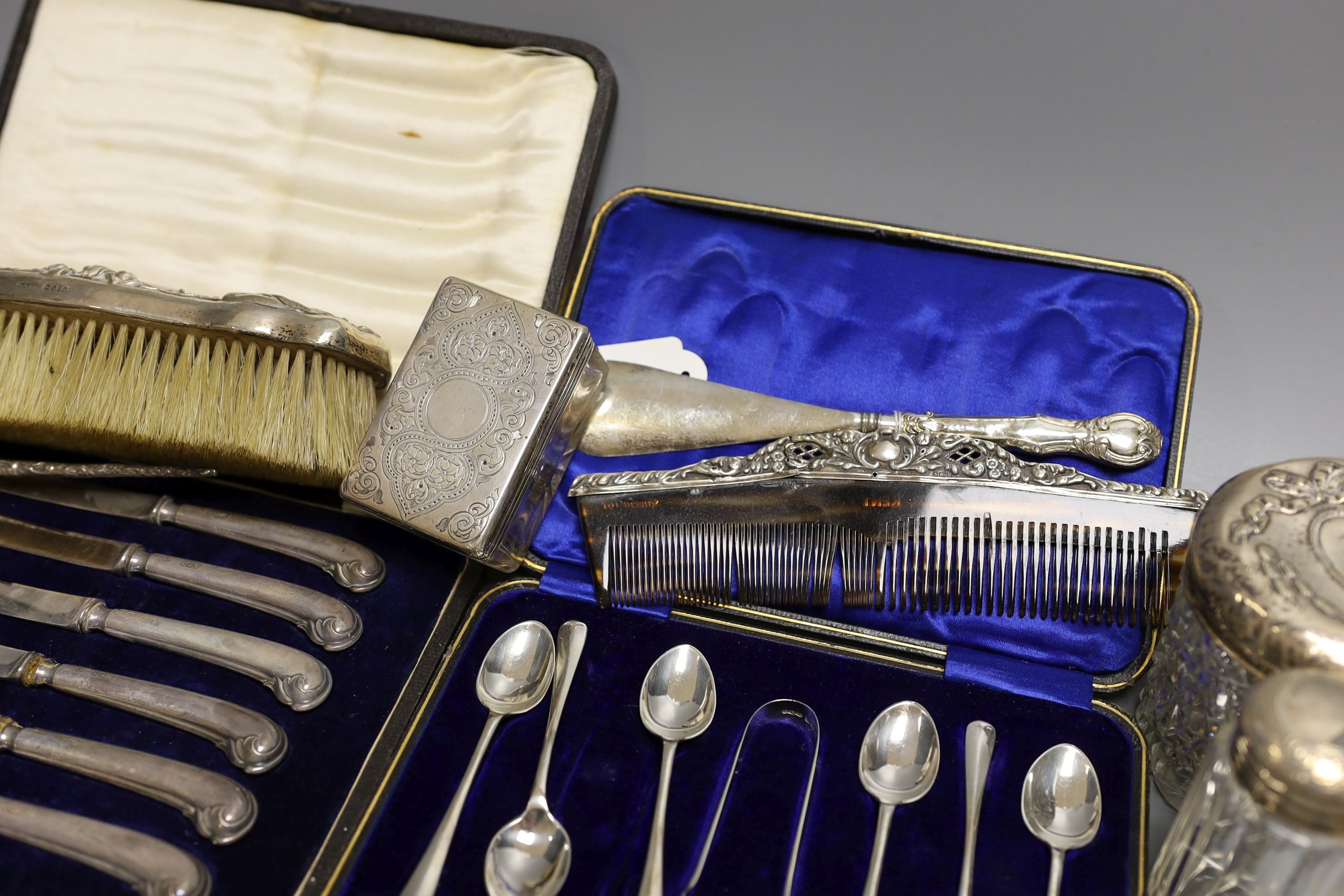 Four assorted silver mounted glass toilet jars, a silver mounted brush, two combs and a shoe horn and two cased sets of cutlery including silver teaspoons with tongs.